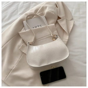 Detail of white crocodile pattern PU leather shoulder bag on a beige blazer and magazines