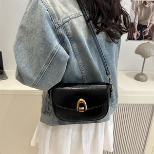 Retro black saddle bag with gold metal U-shaped buckle worn as a crossbody purse