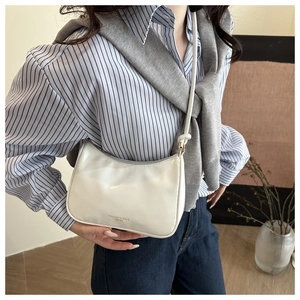 Close-up of cream patent leather baguette bag with gold logo on striped shirt outfit