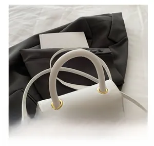 Detail view of white leather handbag with golden bow hardware on stylish blazer