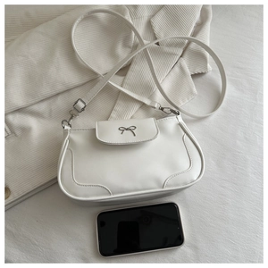 Detailed view of a white PU leather crossbody bag featuring a golden bow lock on corduroy