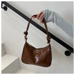 Detail of brown glossy PU leather handbag with knot strap and gold metal buckle