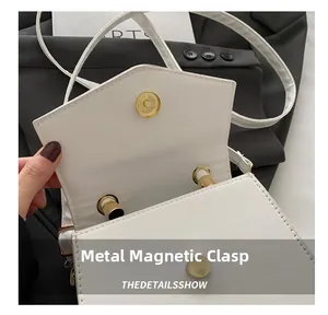 Close-up of golden magnetic metal buckle on a minimalist white leather crossbody bag