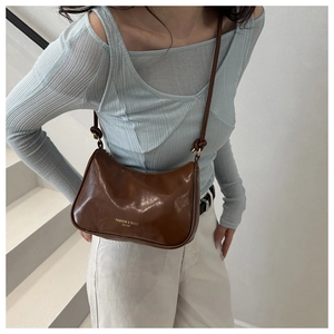 Detail view of brown semi-circle leather shoulder bag with adjustable strap and gold lettering