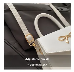 Detail view of white leather handbag featuring golden bow hardware and adjustable strap buckle
