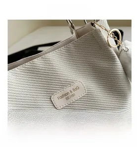 Close-up of cream woven tote bag featuring a leather logo patch and gold chain detail