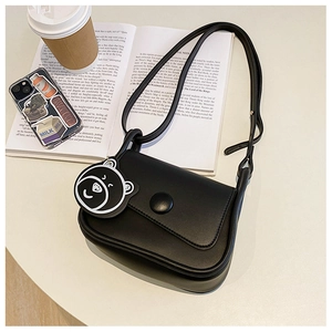 Detail of black mini crossbody bag with cute bear charm on a lifestyle desk background