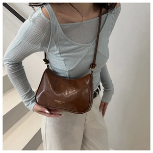 Detail of glossy dark brown leather hobo bag featuring gold lettering and knotted strap