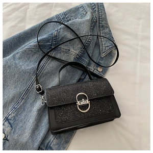 Macro detail of black glitter flap shoulder bag with silver oval twist lock and smooth leather