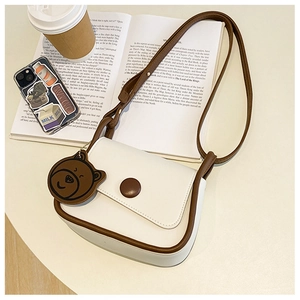 Detail of white leather crossbody bag with brown trim and cute bear charm pendant