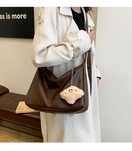 Close-up of large brown leather hobo bag with cute plush cloud charm on a white coat
