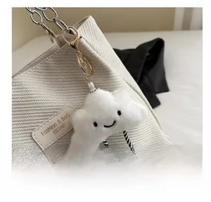 Detail of a white plush cloud charm with smiley face on a canvas tote bag