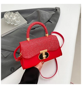 Detail of red glitter crossbody bag with gold twist lock held against a grey suit