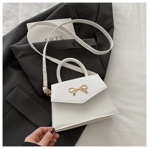 Detail of white mini crossbody bag featuring a golden bow metal lock and trapezoid shape