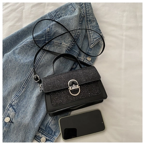 Close-up of black leather crossbody bag with silver oval metal lock and top handle