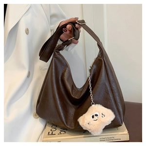 Close-up of dark brown leather tote bag with lychee texture and cute plush charm pendant
