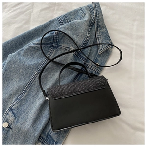 Detailed view of black mini crossbody bag with glitter flap on denim jacket background