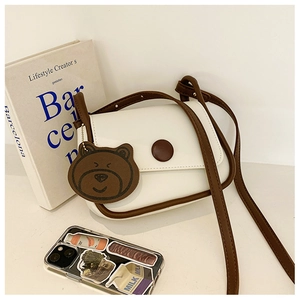 Detail view of a white leather crossbody bag with brown trim and cute bear charm decoration