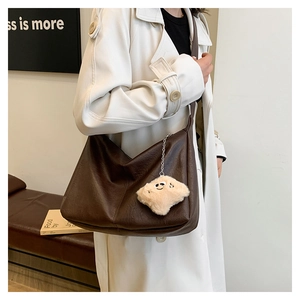 Detail of soft brown leather tote bag with plush smiley charm and wide shoulder strap
