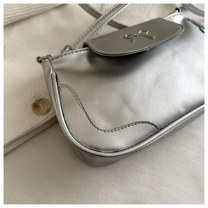 Close-up of metallic silver shoulder bag featuring a decorative metal bow clasp