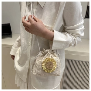 Detail of a woven straw bucket bag featuring a large sunflower ornament and drawstring closure
