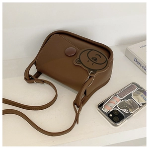 Detail of a brown leather crossbody bag with a cute bear tag and magnetic snap button
