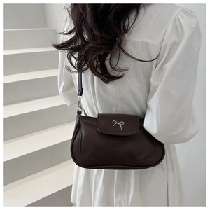 Model wearing dark brown vintage shoulder bag with silver bow on a white staircase