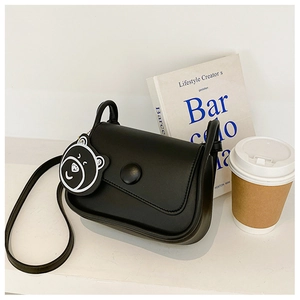 Detail shot of a black matte leather shoulder bag with a bear charm and round buckle