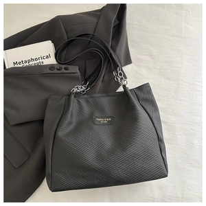 Détail du cabas noir texturé avec plaque logo métallique et bandoulière en chaîne