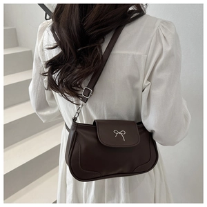 Detail of dark brown PU leather crossbody bag featuring a silver metal bow buckle