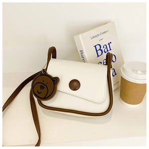 Close-up of a cream-colored saddle bag with brown trim and a cute bear charm