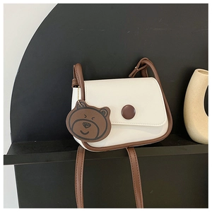Detail of a creamy white mini crossbody bag with brown trim and cute bear charm accent