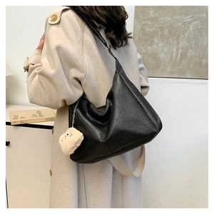 Detail of a large black soft leather hobo bag featuring a cute beige teddy bear charm