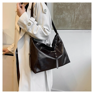 Side view of large dark brown leather hobo bag worn by model in long white coat