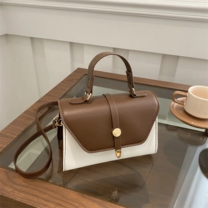 Sac bandoulière en cuir marron et blanc avec boucle dorée sur table de café en bois