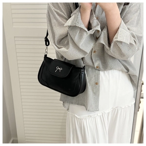 Close-up of black retro shoulder bag with silver bow buckle on white skirt backdrop