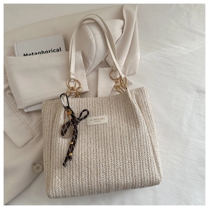 Close-up of beige woven tote bag with leather strap and decorative tennis racket charm