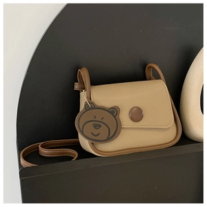 Detail of minimalist beige square crossbody bag with brown buckle and bear charm