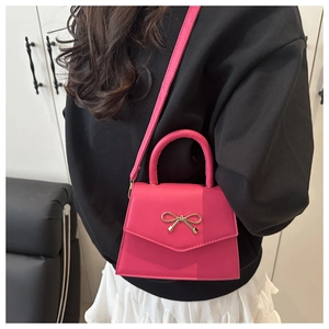 Detailed view of a fuchsia mini handbag with golden bow buckle on black clothing