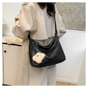 Close-up of black textured tote bag featuring a cute white plush bear charm accessory