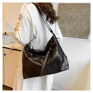 Detail of a black glossy leather tote bag showing large capacity on a model wearing white