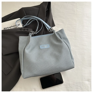Détail du cabas tissé bleu clair avec bandoulière en chaîne et étiquette sur tissu beige