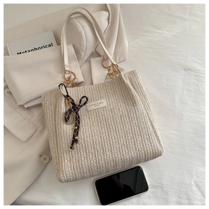 Detail of beige woven straw tote bag featuring ribbon bow and size reference with smartphone