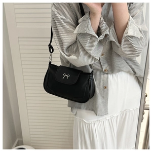 Close-up of black retro shoulder bag with silver bow buckle worn on person