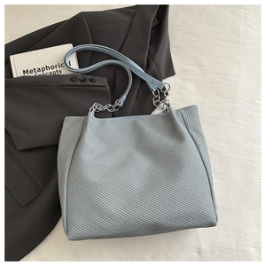 Détail du sac cabas en tweed bleu clair avec chaîne argentée et texture tissée élégante