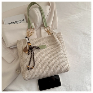 Detail of straw woven tote bag with green leather handles and metal hardware accents