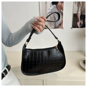 Detail shot of black crocodile embossed shoulder bag held by hand in a home setting