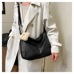 Detail of a black leather Hobo tote bag with a plush charm on a beige trench coat