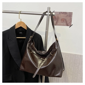 Detail of dark brown glossy leather tote bag with metal buckle on a black blazer