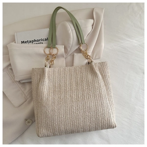Detail of woven straw tote bag featuring mint green leather straps and gold metal rings